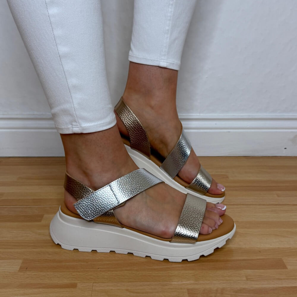 Oh My Sandals 5951 Gold sandals worn with white pants on a wooden floor.