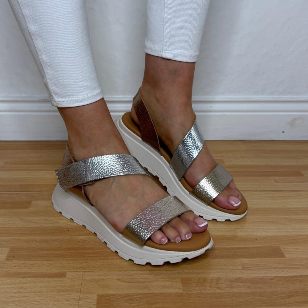 Oh My Sandals 5951 Gold sandals worn with white pants on a wooden floor.