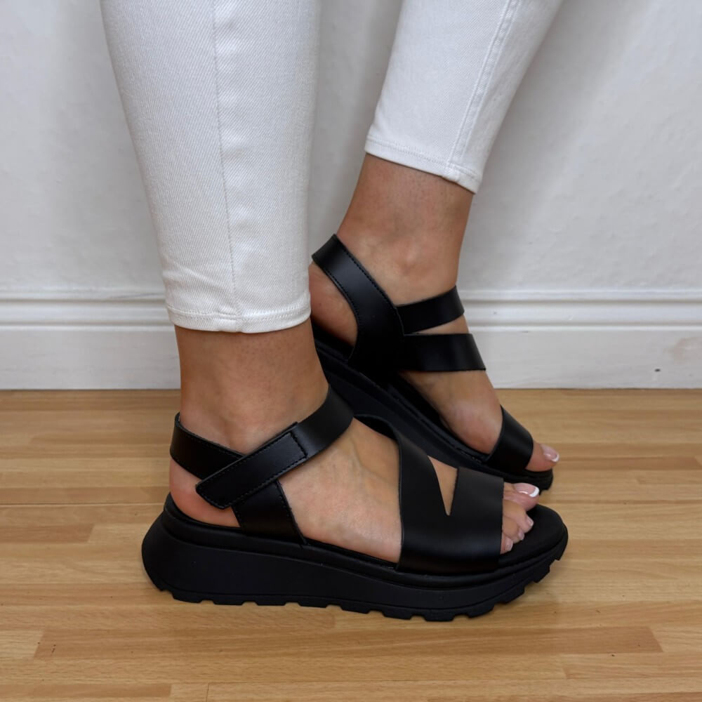 Oh My Sandals 5955 Black sandals worn with white pants on a wooden floor.