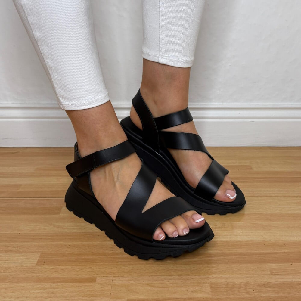 Oh My Sandals 5955 Black sandals worn with white pants on a wooden floor.