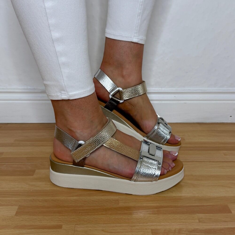 Oh My Sandals 5961 Gold and silver platform sandals worn with white pants on a wooden floor. 