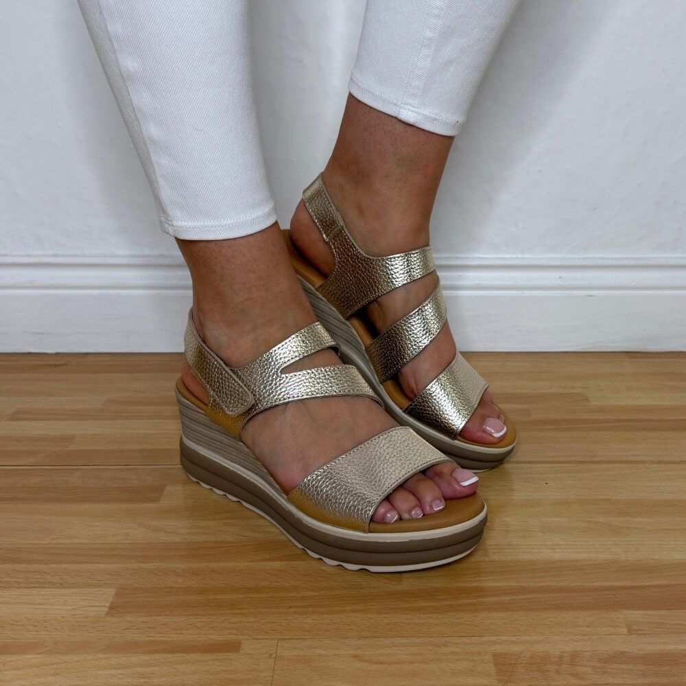 Oh My Sandals 5990 Gold wedge sandals worn with white pants on a wooden floor.