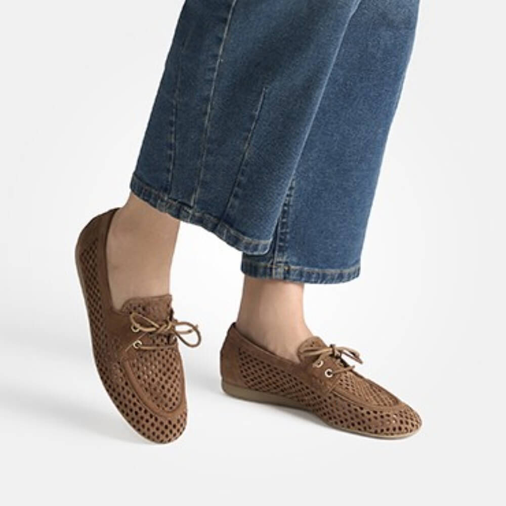 Brown perforated loafers worn with blue jeans on a light gray background