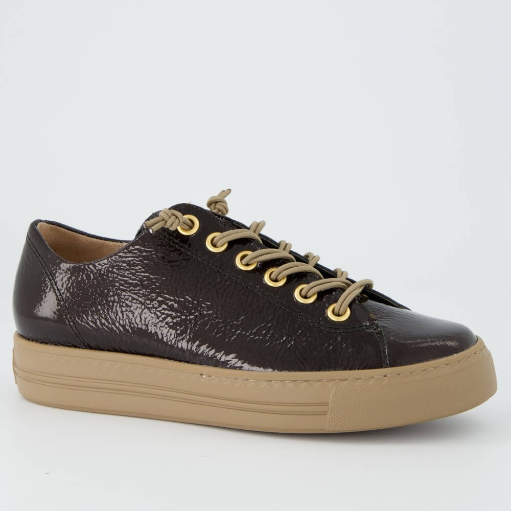 A Paul Green low-top sneaker in glossy dark brown textured leather with beige laces threaded through gold-tone eyelets and a thick beige rubber sole, shown on a light grey background.