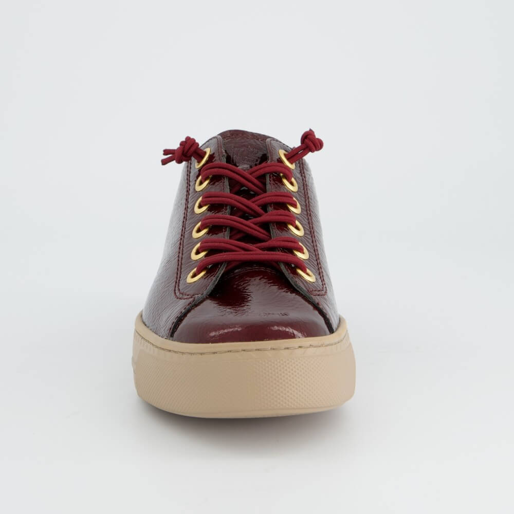 A Paul Green low-top leather sneaker in a deep burgundy red with matching red laces threaded through gold-tone eyelets, featuring a thick beige platform sole, shown against a plain light grey background.