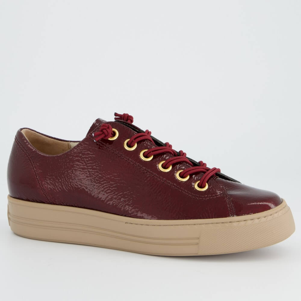 A Paul Green low-top leather sneaker in a deep burgundy red with matching red laces threaded through gold-tone eyelets, featuring a thick beige platform sole, shown against a plain light grey background.