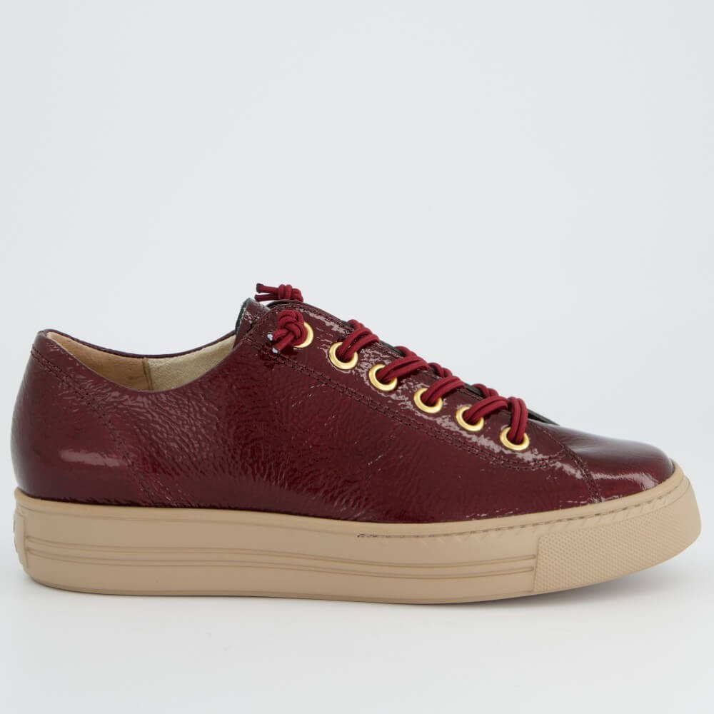 A Paul Green low-top leather sneaker in a deep burgundy red with matching red laces threaded through gold-tone eyelets, featuring a thick beige platform sole, shown against a plain light grey background.