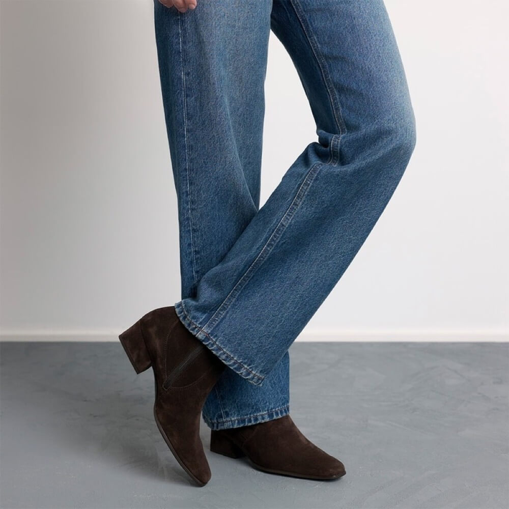 Person wearing blue jeans and Paul Green dark brown suede ankle boots with a low block heel and pointed toe