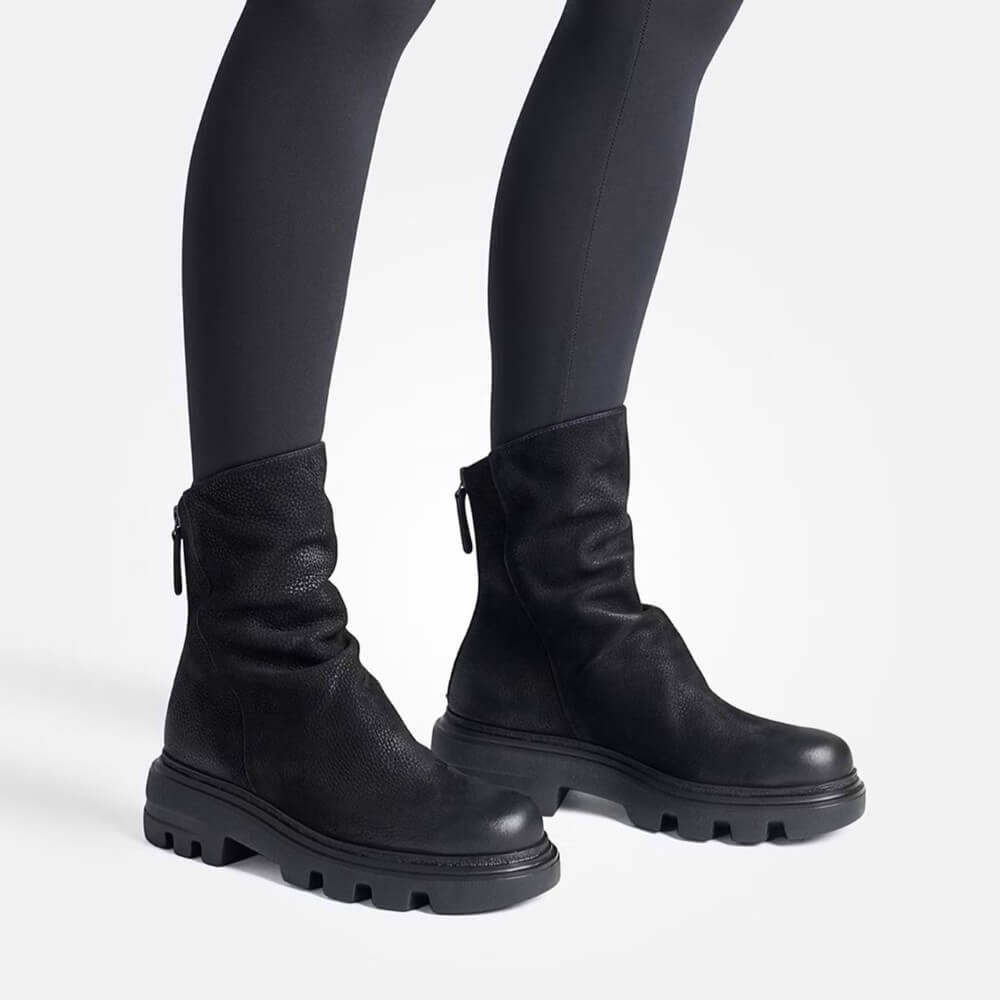 Black leather boots worn with black leggings on a white background