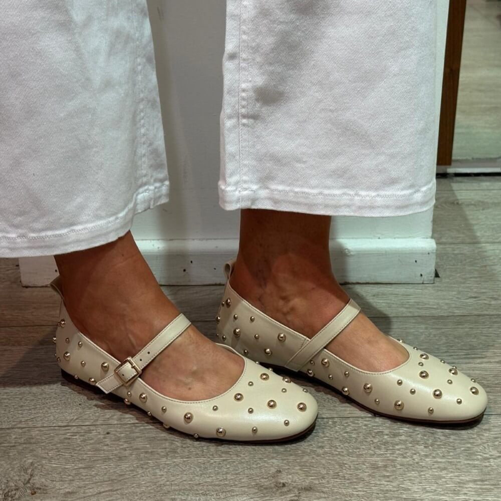 Pedro Anton Beige studded flats worn with light-coloured pants on a wooden floor.