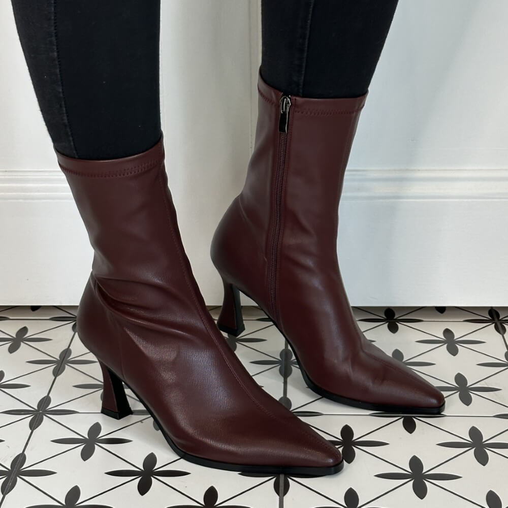 Burgundy high-heeled boots worn with black pants on a tiled floor.