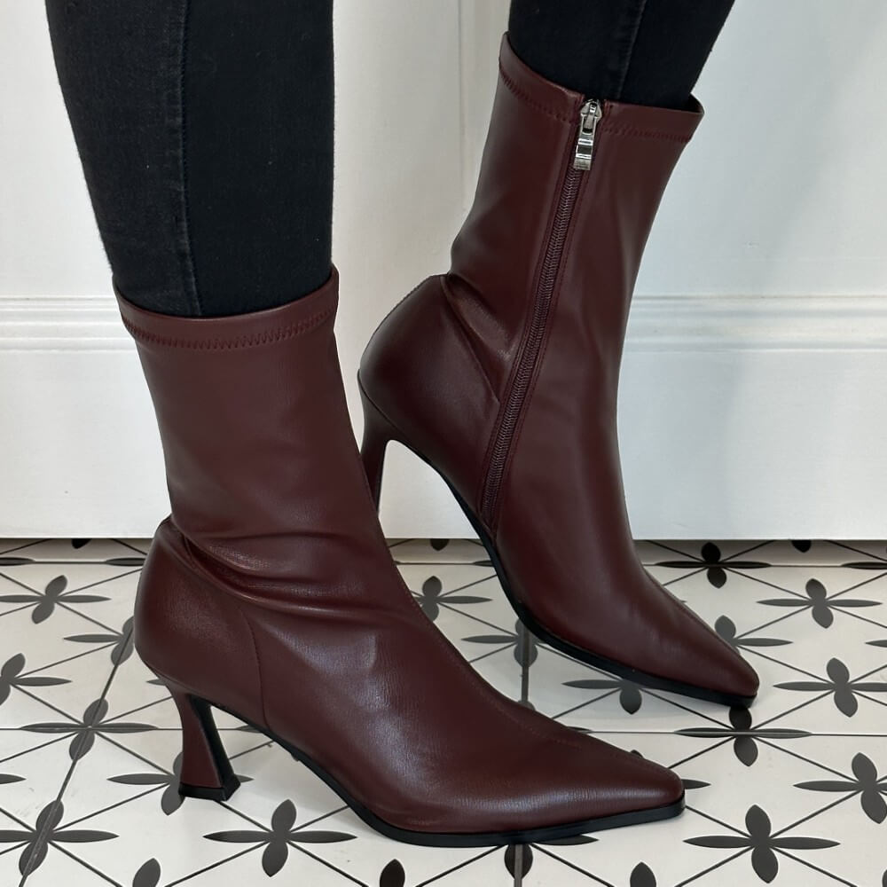 Burgundy high-heeled boots worn with black pants on a tiled floor.