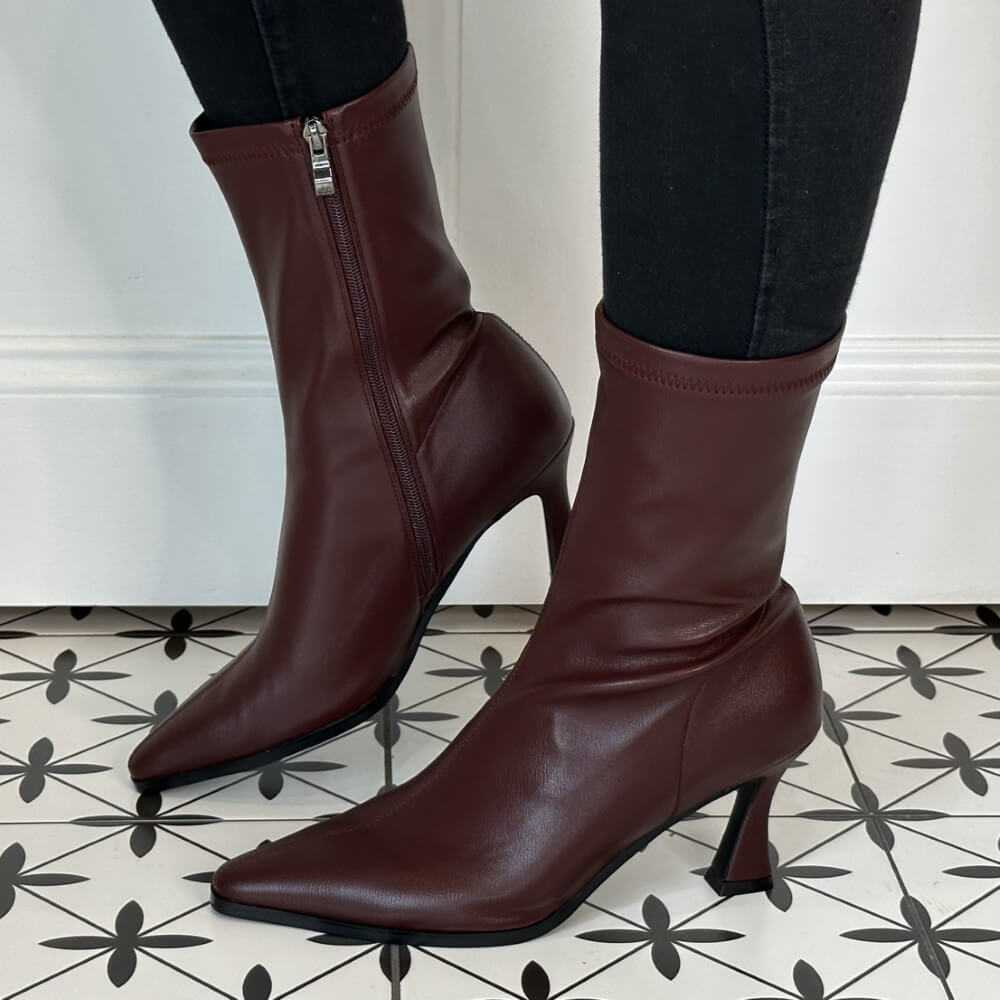 Burgundy high-heeled boots worn with black pants on a tiled floor.