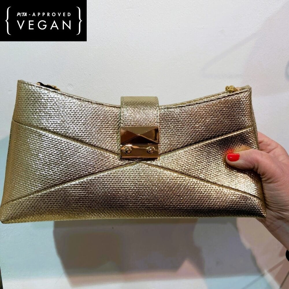 Pepe Moll Gold clutch held   against a light background, featuring 'PETA-Approved Vegan' label.