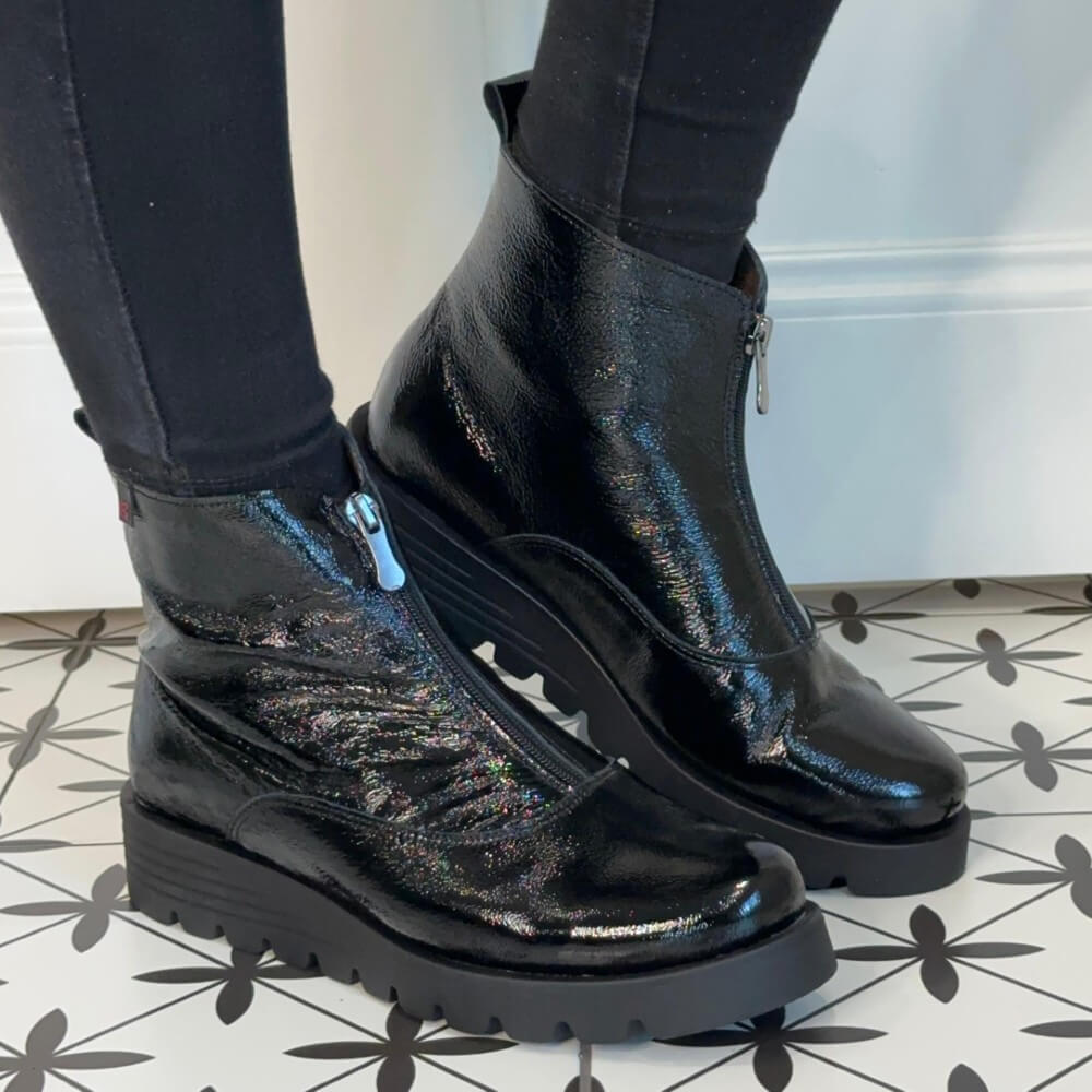 Black patent boots worn with black pants on a patterned floor. Pepe Saenz Wedge Patent Leather Ankle Boots 21544 Black