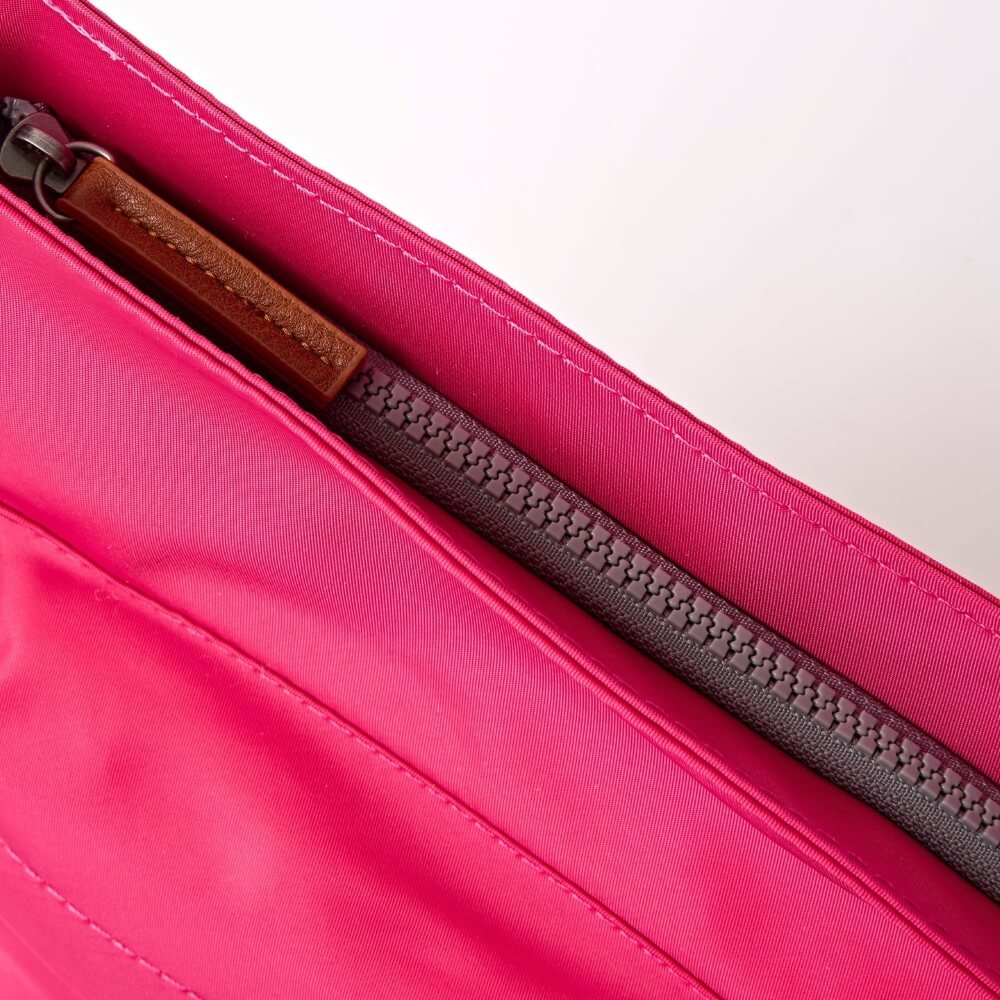 Close-up of a pink bag with a zipper and brown pull tab on a white background