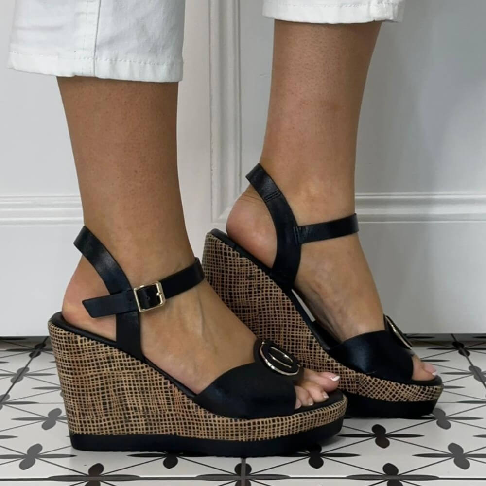 Repo Black wedge sandals with a patterned sole worn by a person on a tiled floor.