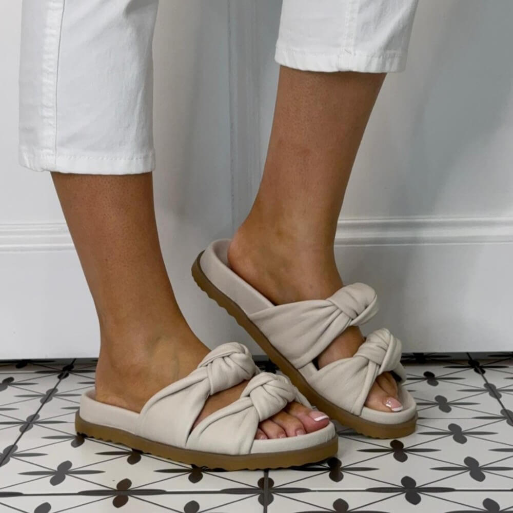 Repo Ivory Leather  sandals with knot details worn by a person on a patterned floor.