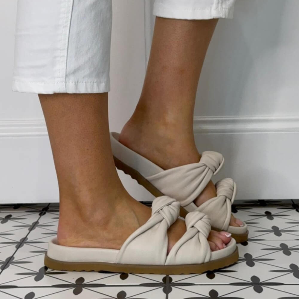 Repo Ivory Leather  sandals with knot details worn by a person on a patterned floor.
