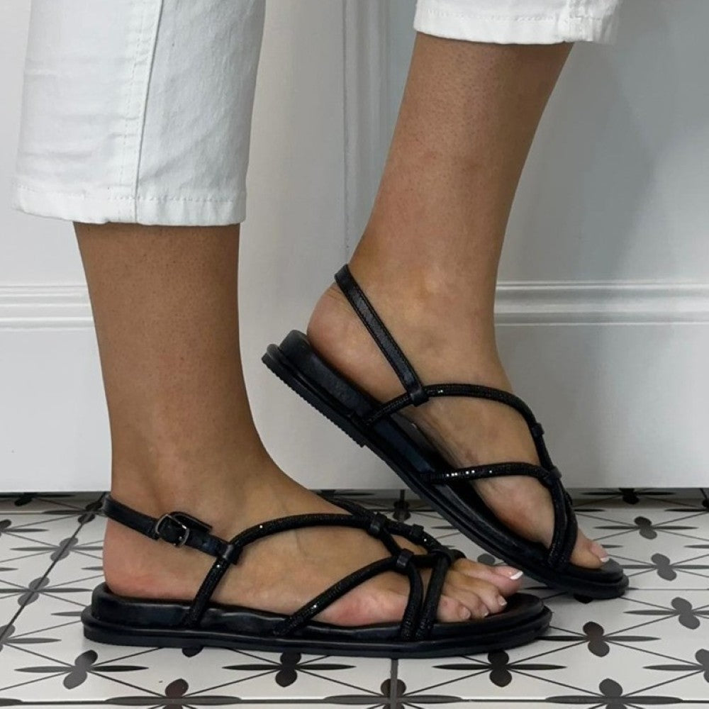 Repo Black strappy sandals worn with white pants on a tiled floor.