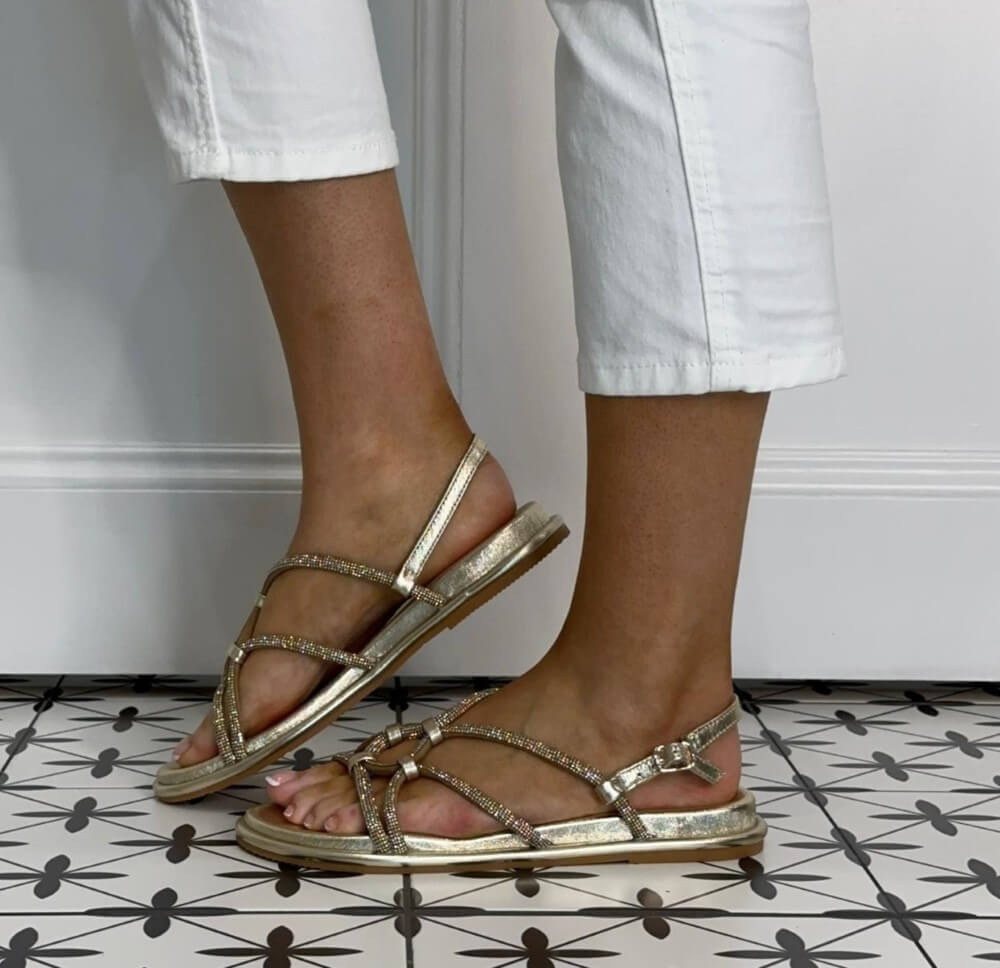Repo Gold strappy sandals worn with white pants on a tiled floor.