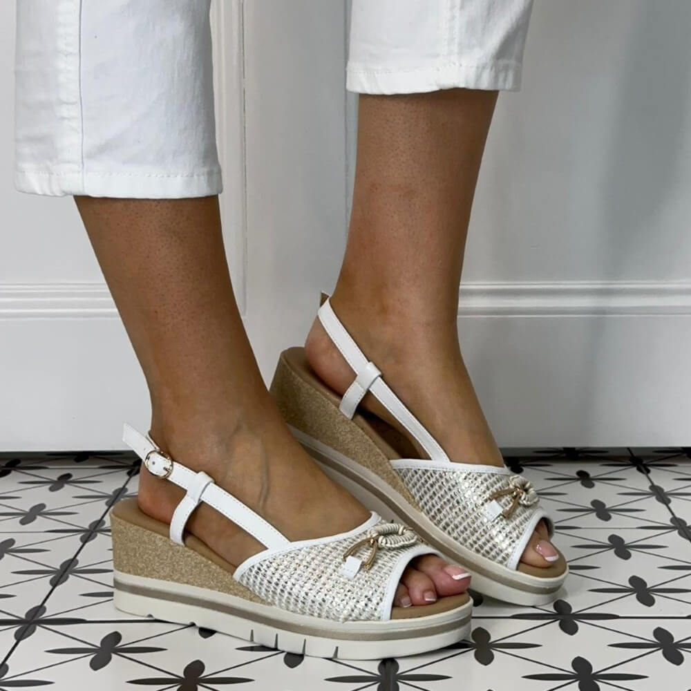 Repo White wedge sandals with gold accents worn by a person on a patterned floor.