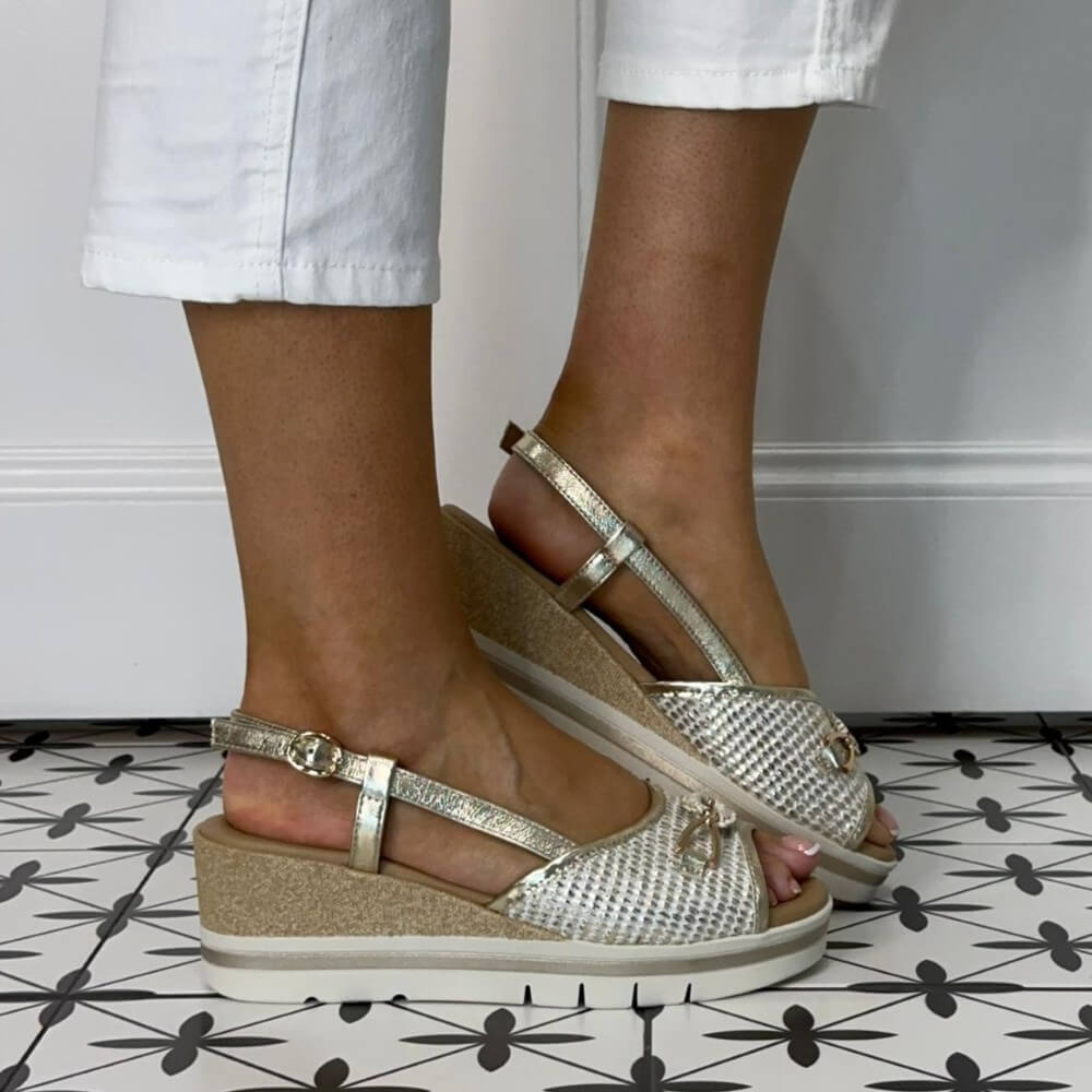 Repo Gold wedge sandals worn with white pants on a patterned floor.