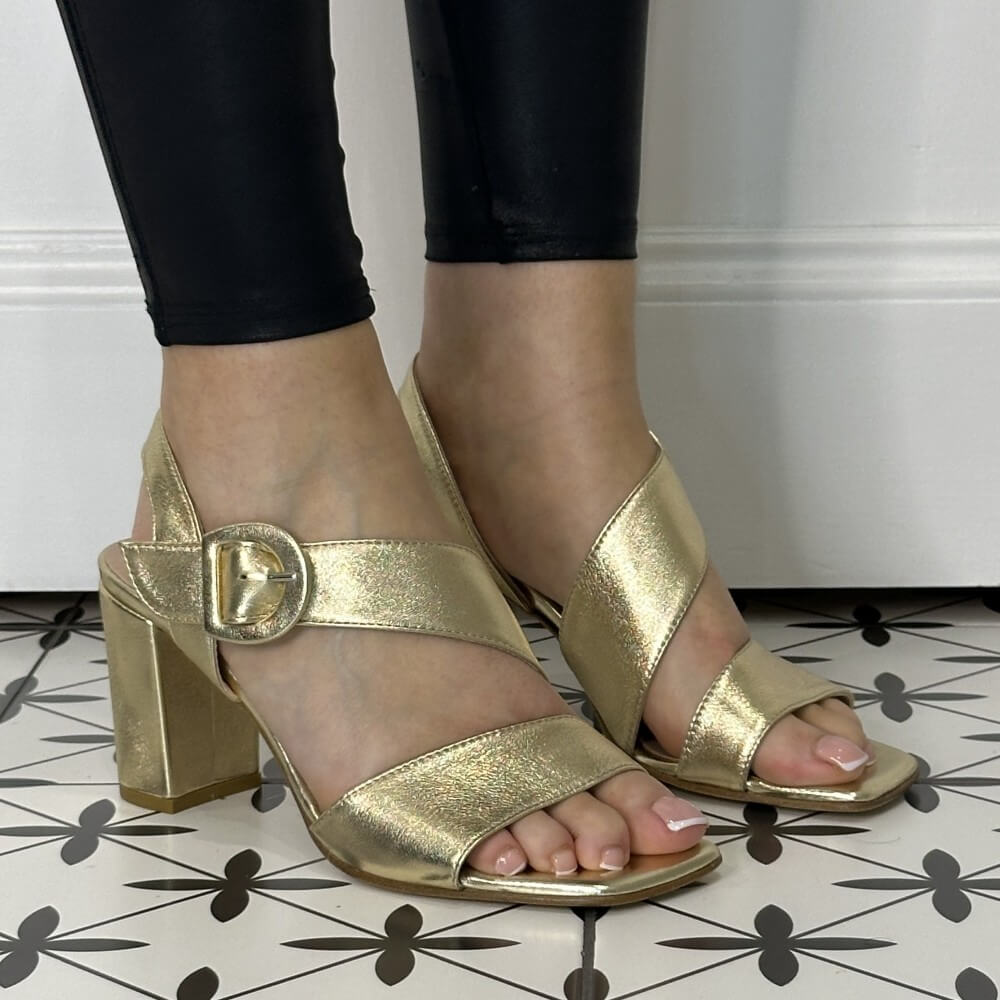 Repo 39626 Gold high-heeled sandals worn with black pants on a patterned floor.
