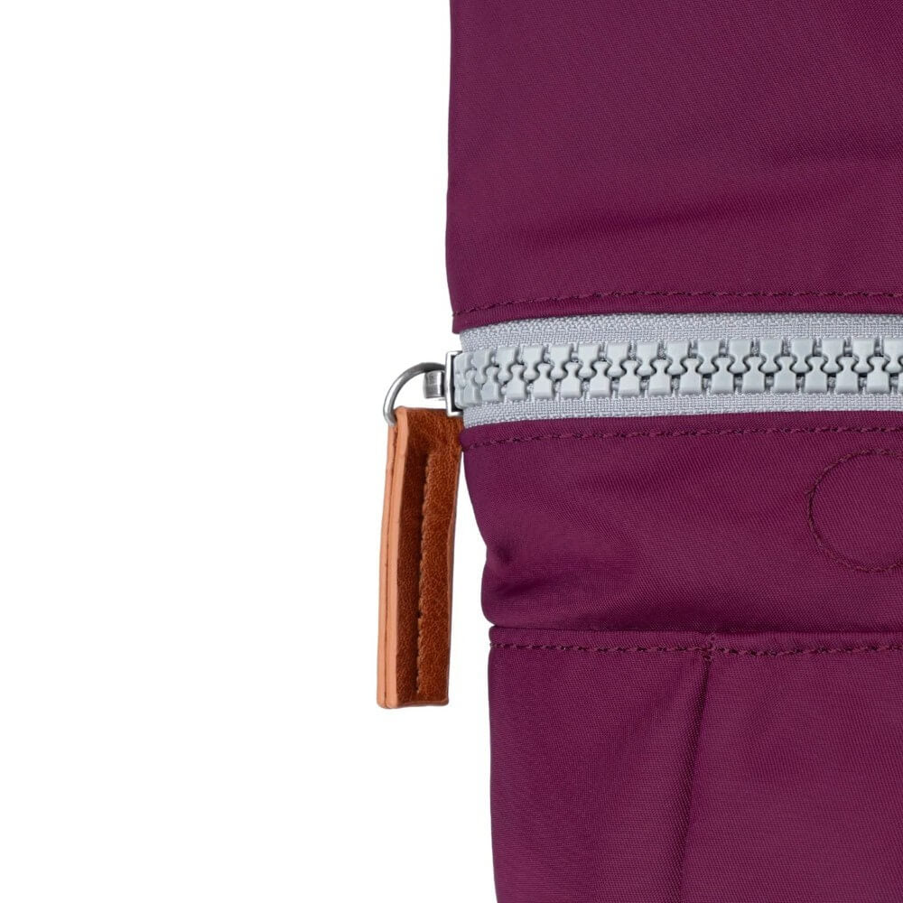 Close-up of a purple rucksack with a zipper and brown leather pull tab on a white background