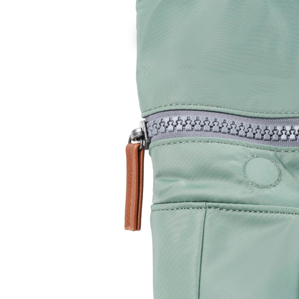 Close-up of a light green jacket with a zipper and brown pull tab on a white background