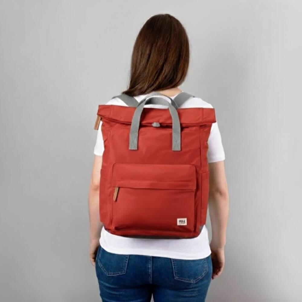 Person wearing a red backpack with gray straps on a plain background