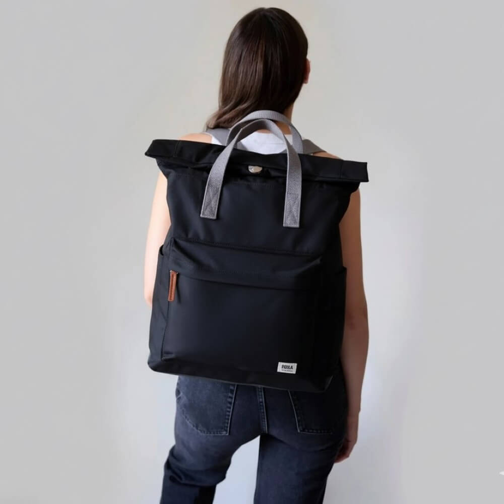 Person wearing a black backpack with gray straps against a plain background