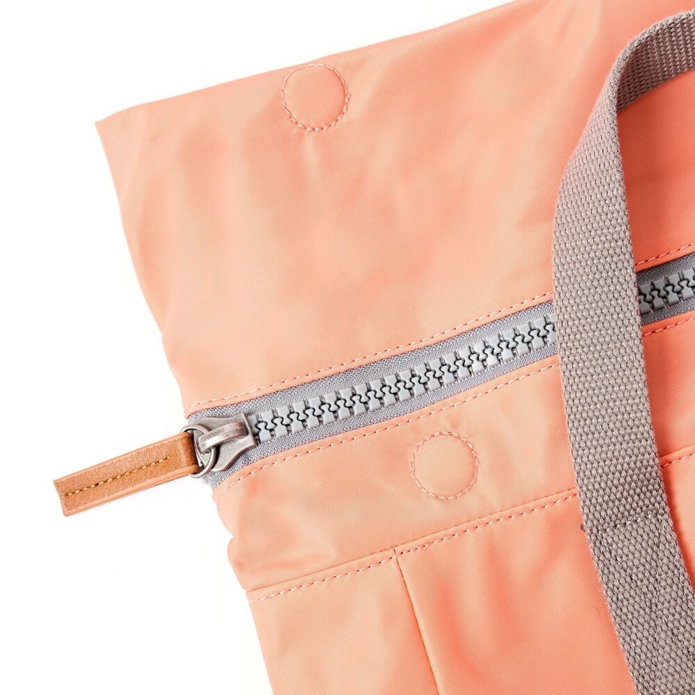 Close-up of a peach-colored bag with a zipper and strap on a white background
