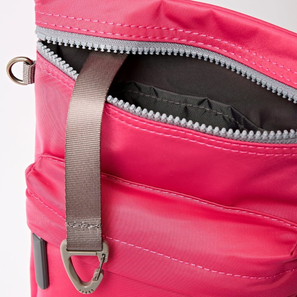 Close-up of a Roka pink bag with a grey strap and carabiner on a white background