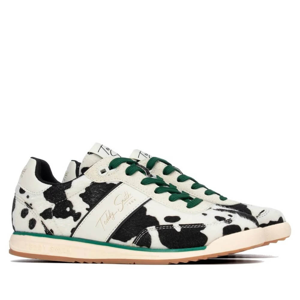 A pair of Teddy Smith low-top sneakers featuring a black and white cow print pattern, dark green laces, a green stripe along the side, and a light beige midsole with a gum outsole.