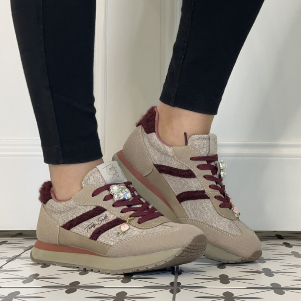 A person wearing Teddy Smith beige and burgundy low-top sneakers with black leggings, standing on a black-and-white patterned tile floor against a white wall.