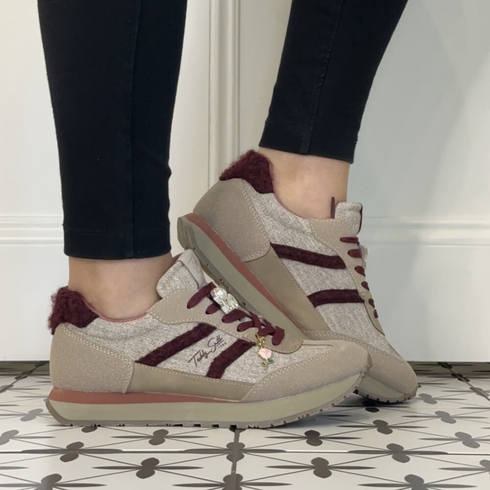 A person wearing Teddy Smith beige and burgundy low-top sneakers with black leggings, standing on a black-and-white patterned tile floor against a white wall.