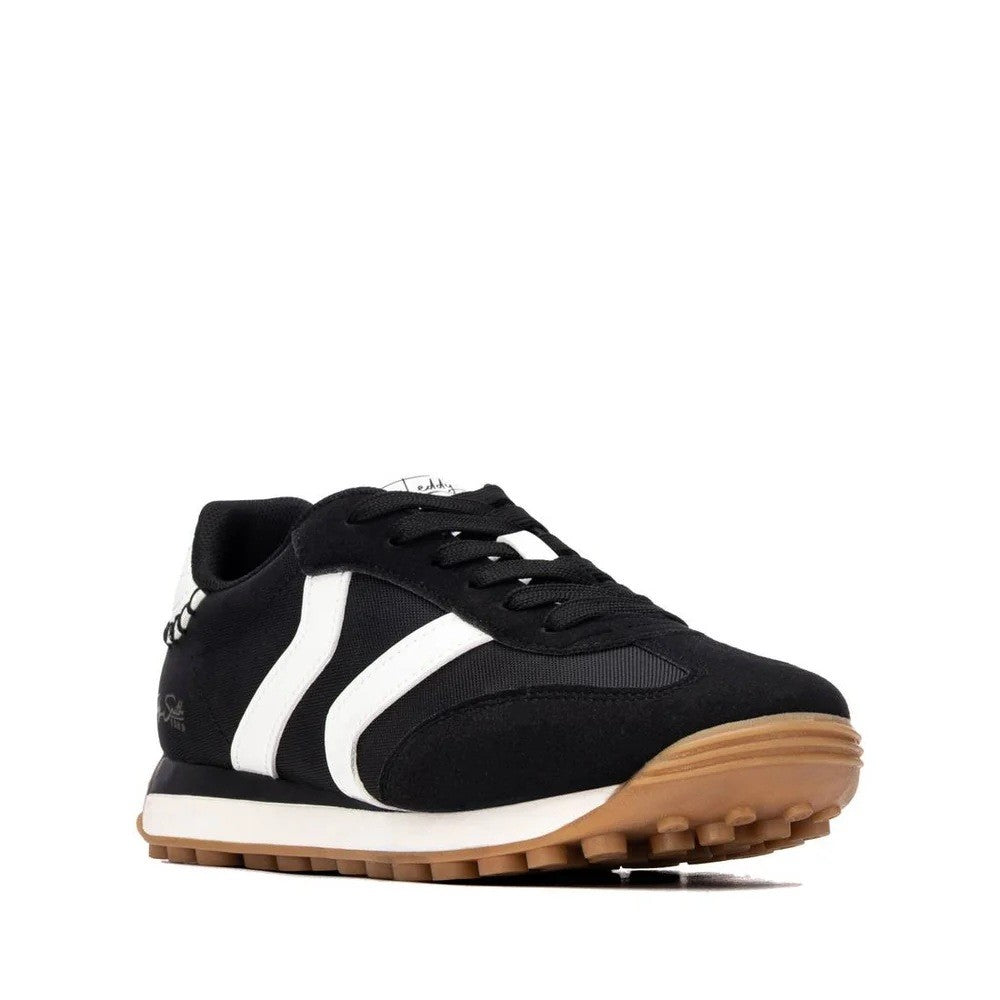 A black low-top sneaker with white side stripes, black laces, a white midsole, and a brown gum outsole, shown from a side profile on a white background.