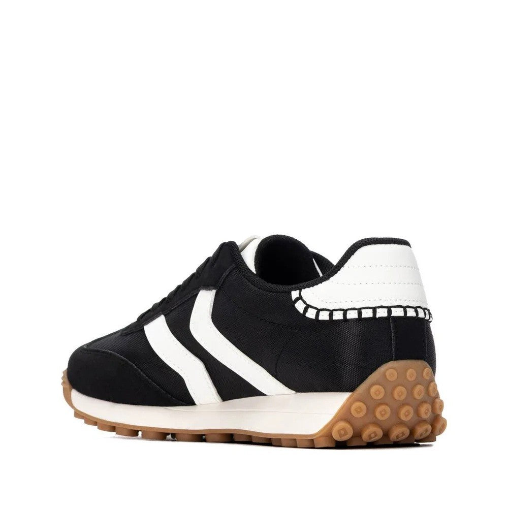 A black and white low-top sneaker with a distinctive brown gum sole, shown from a side profile view on a white background.