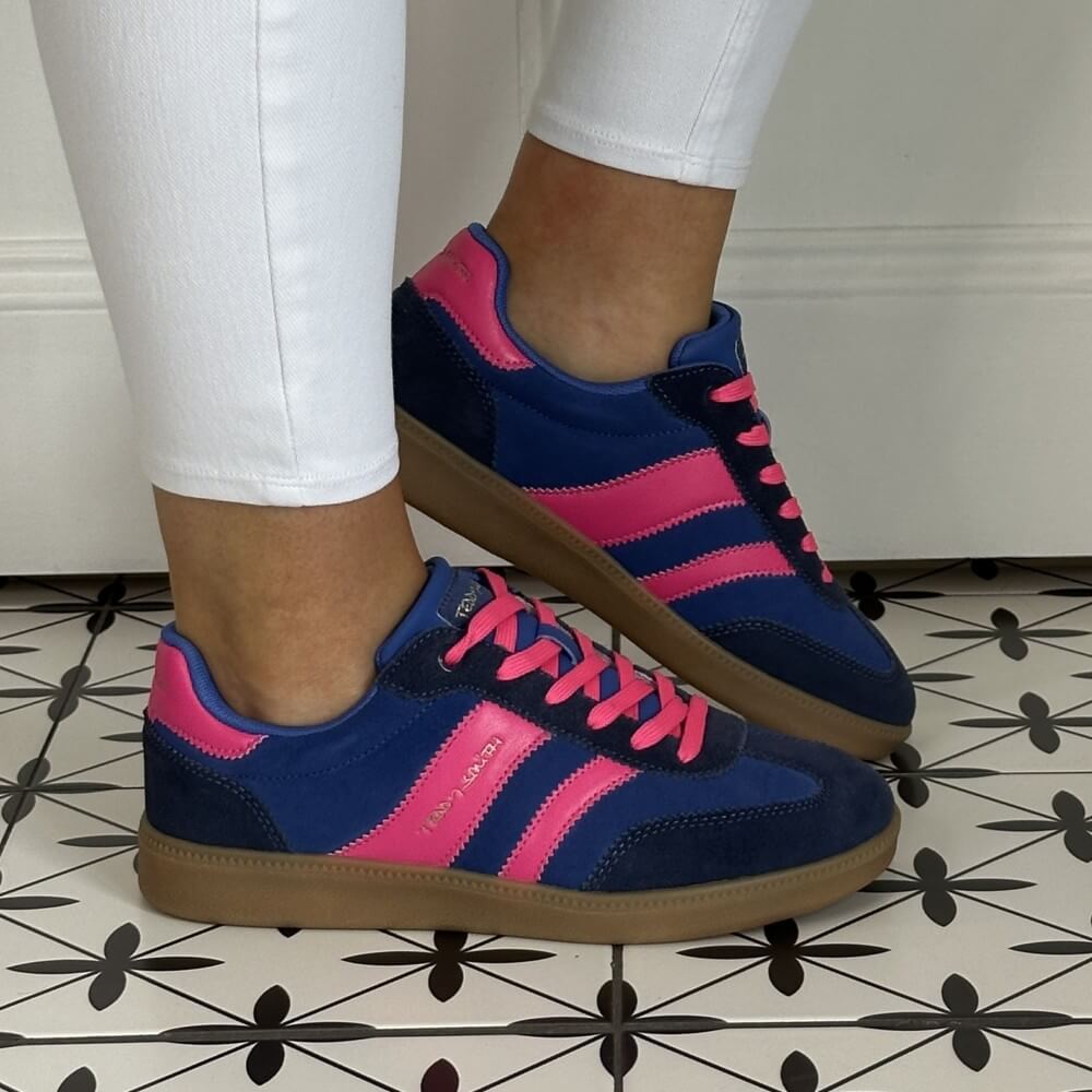 Navy and pink sneakers with brown soles worn indoors on a patterned floor.
