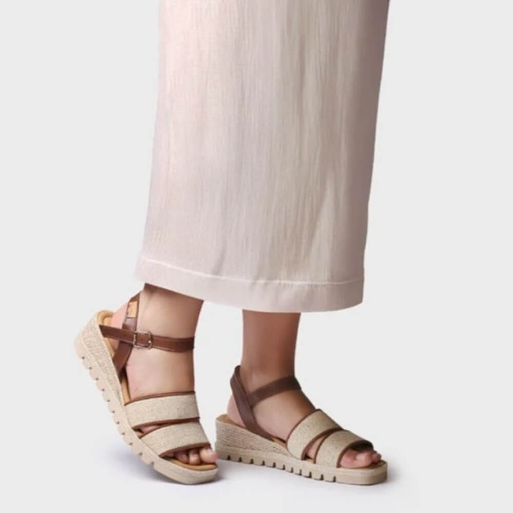 Beige sandals with brown straps worn by a person on a light gray background