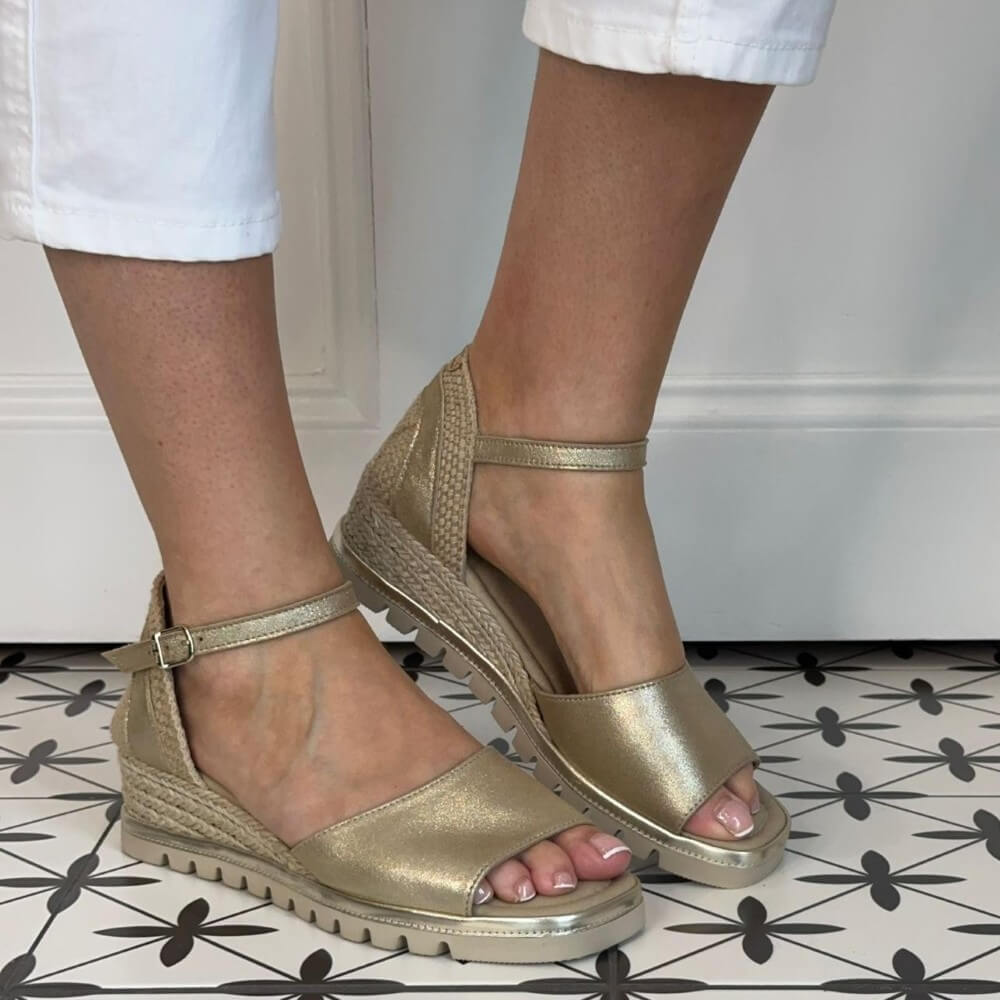 Toni Pons Gold wedge sandals worn with white pants on a patterned floor.