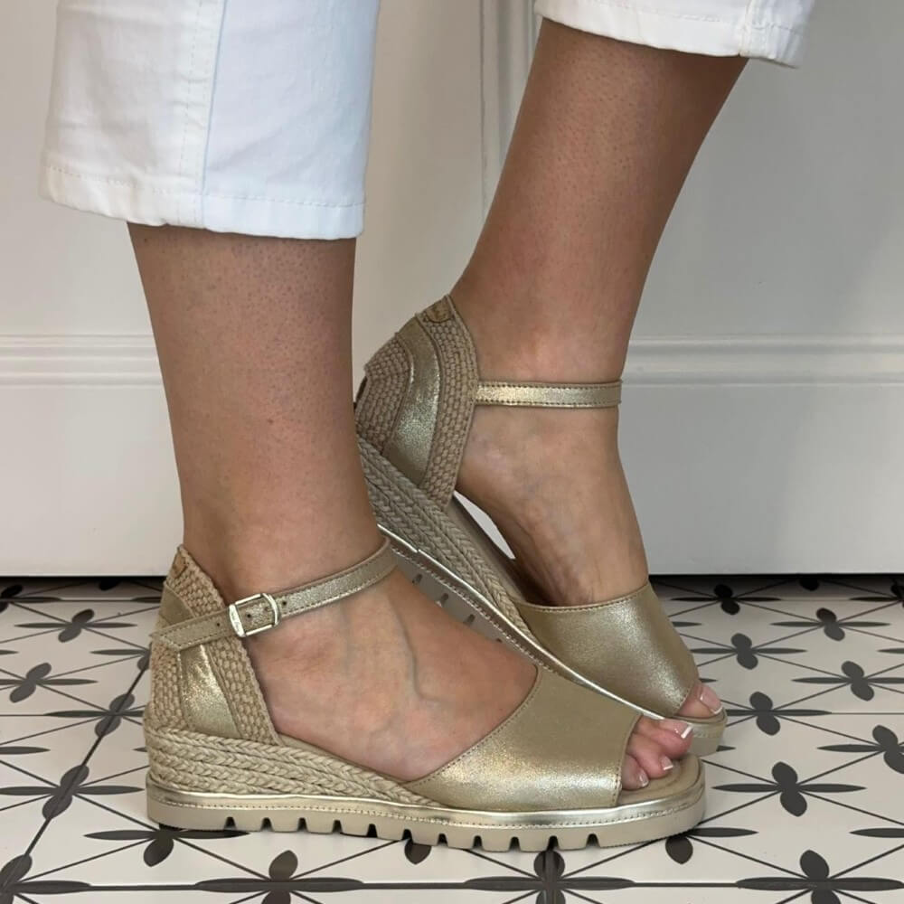 Toni Pons Gold wedge sandals worn with white pants on a patterned floor.