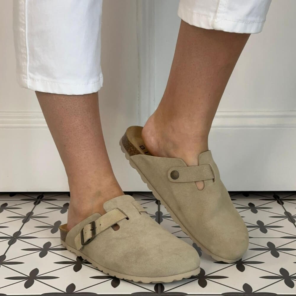 Toni Pons Beige clogs worn with white pants on a patterned floor.