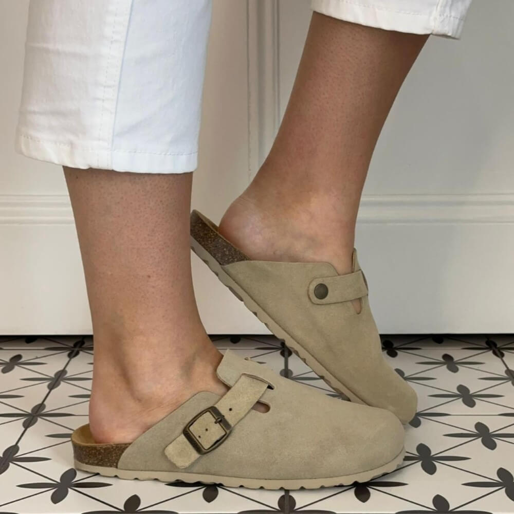Toni Pons Beige clogs worn with white pants on a patterned floor.