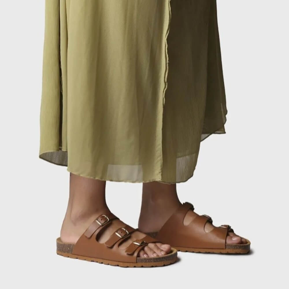Brown sandals worn with a green skirt on a light gray background