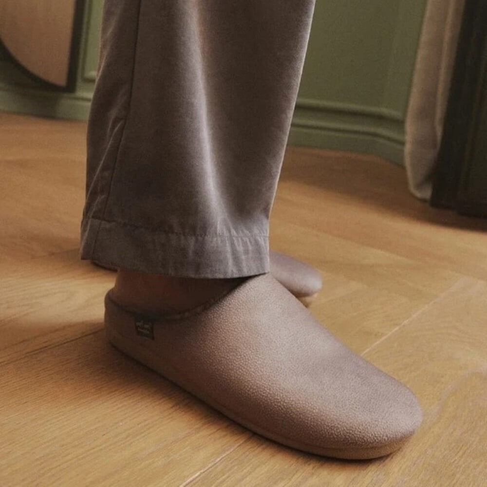 A person wearing Toni Pons  taupe-brown suede slip-on Slippers, standing on a light wood floor.