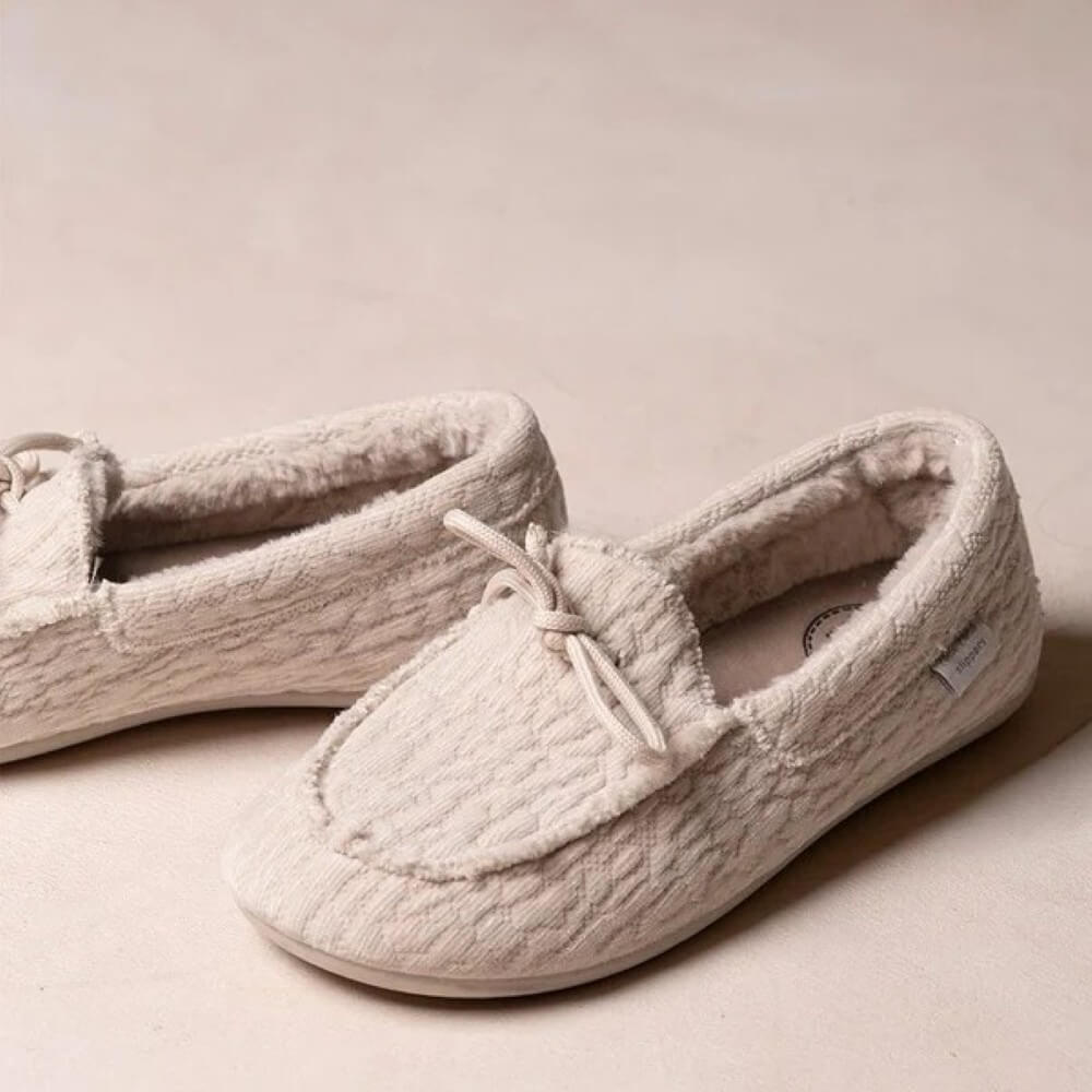 A pair of Toni Pons slip-on slippers in a light beige or cream colour, featuring a textured knit pattern, a small bow on the front, and a soft fleece lining, set against a matching neutral background.