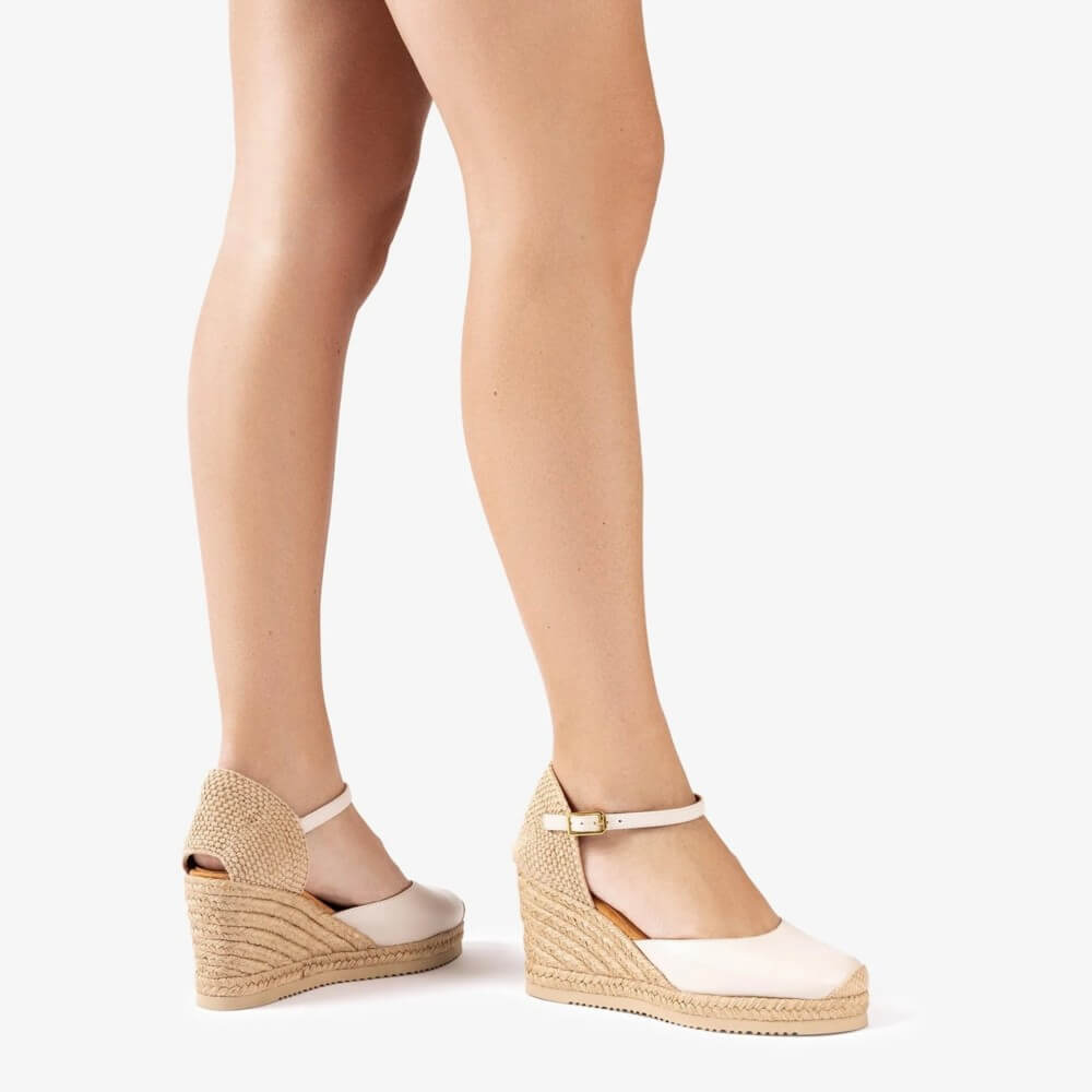 ivory wedge sandals with espadrille sole worn by a person on a white background