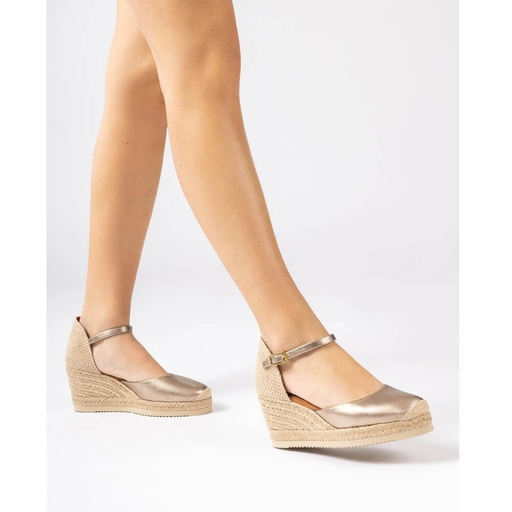 Person wearing Unisa Gold wedge sandal with metallic strap on a white background